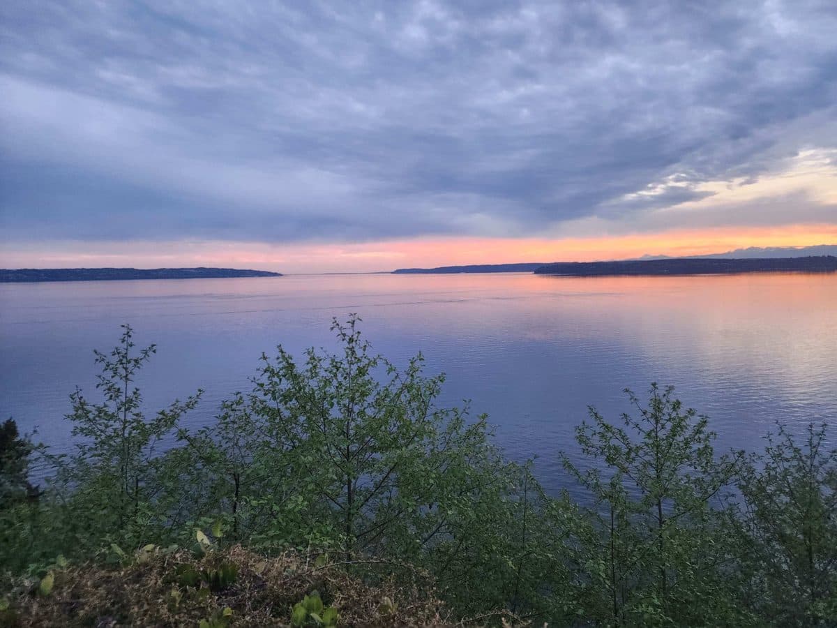 Orange and pink sunset reflecting on calm Puget Sound water from the deck